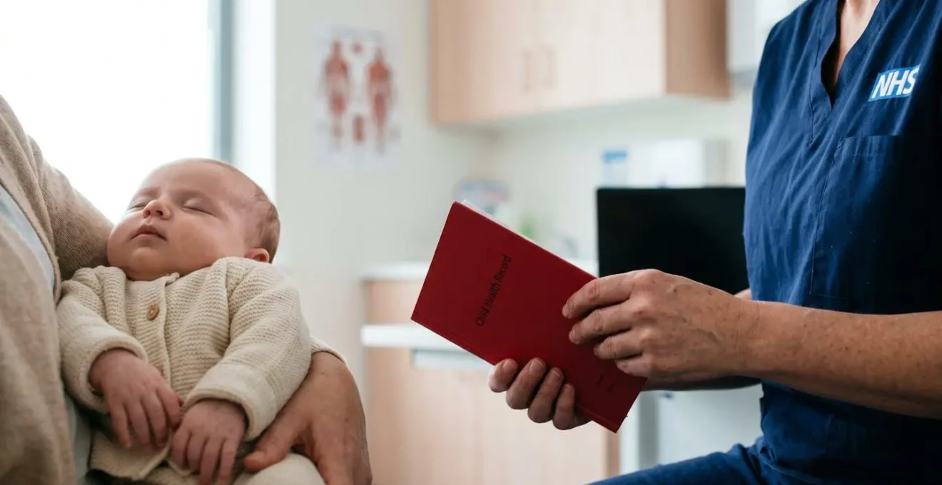 A newborn baby being gently cradled during a health visitor consultation, symbolizing precise timing of NHS vaccination schedule