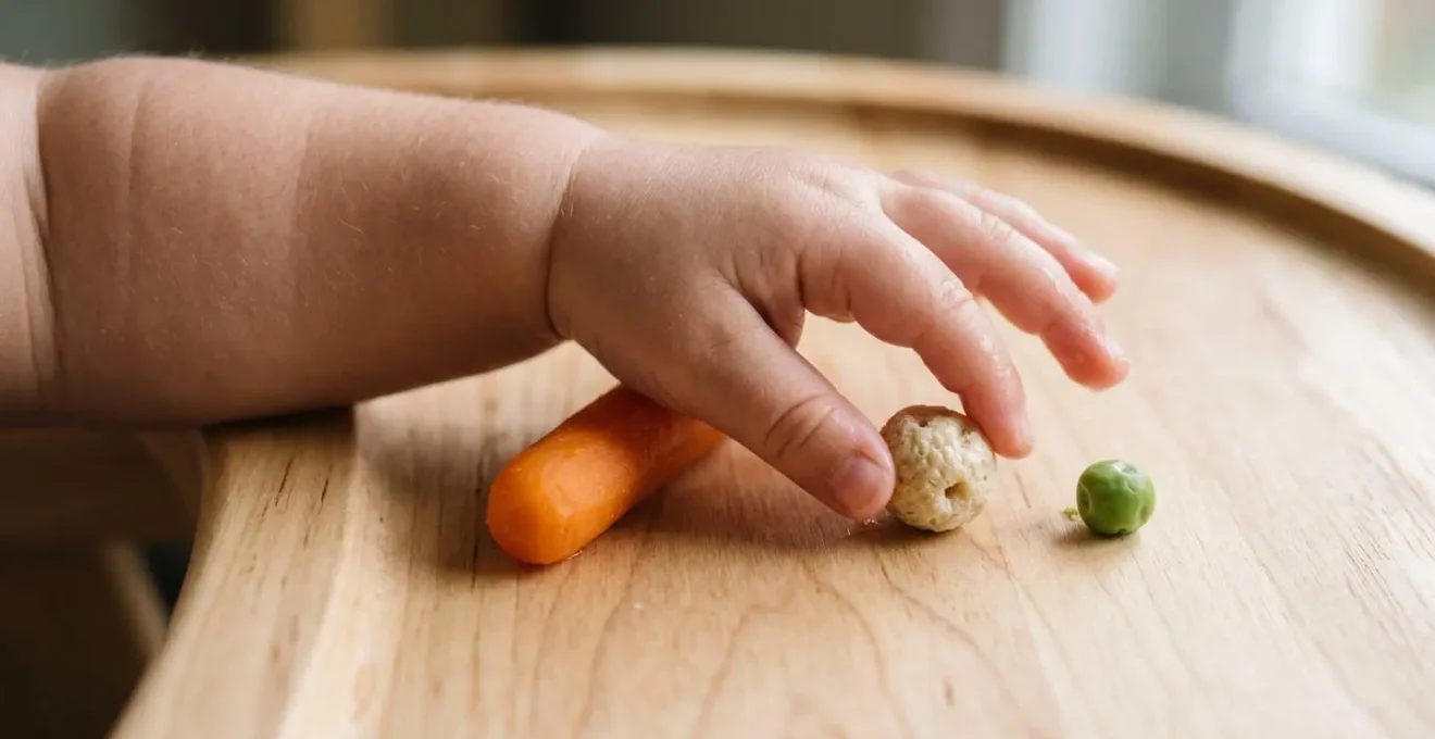 Macro detail of baby fingers progressing from grasping larger soft food to precise pincer grip on small puff cereal