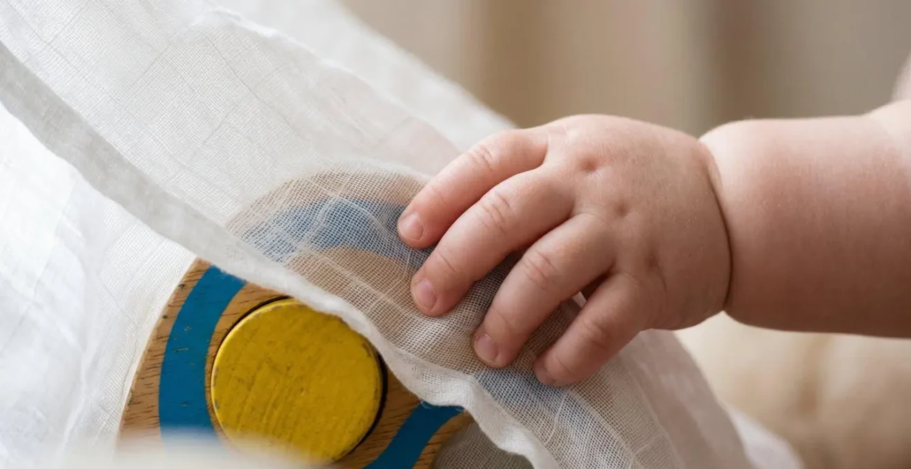 Baby reaching for toy partially hidden under transparent fabric during object permanence game