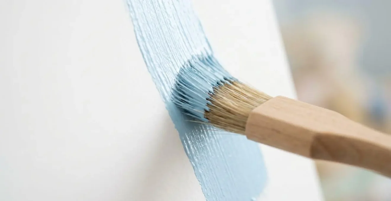Close-up of paintbrush applying white low-VOC paint to nursery wall showing smooth texture and natural finish