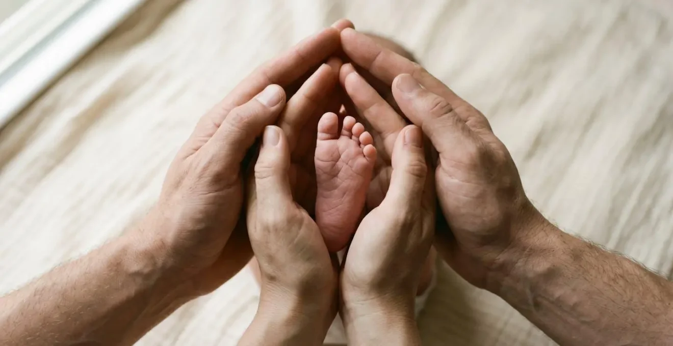 Intimate close-up of two parents' hands gently cradling their newborn baby's tiny foot together symbolizing shared parental partnership